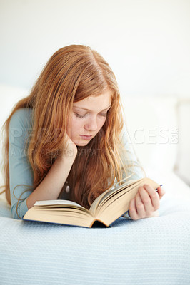 Buy stock photo A young girl reading her book while lying on her bed