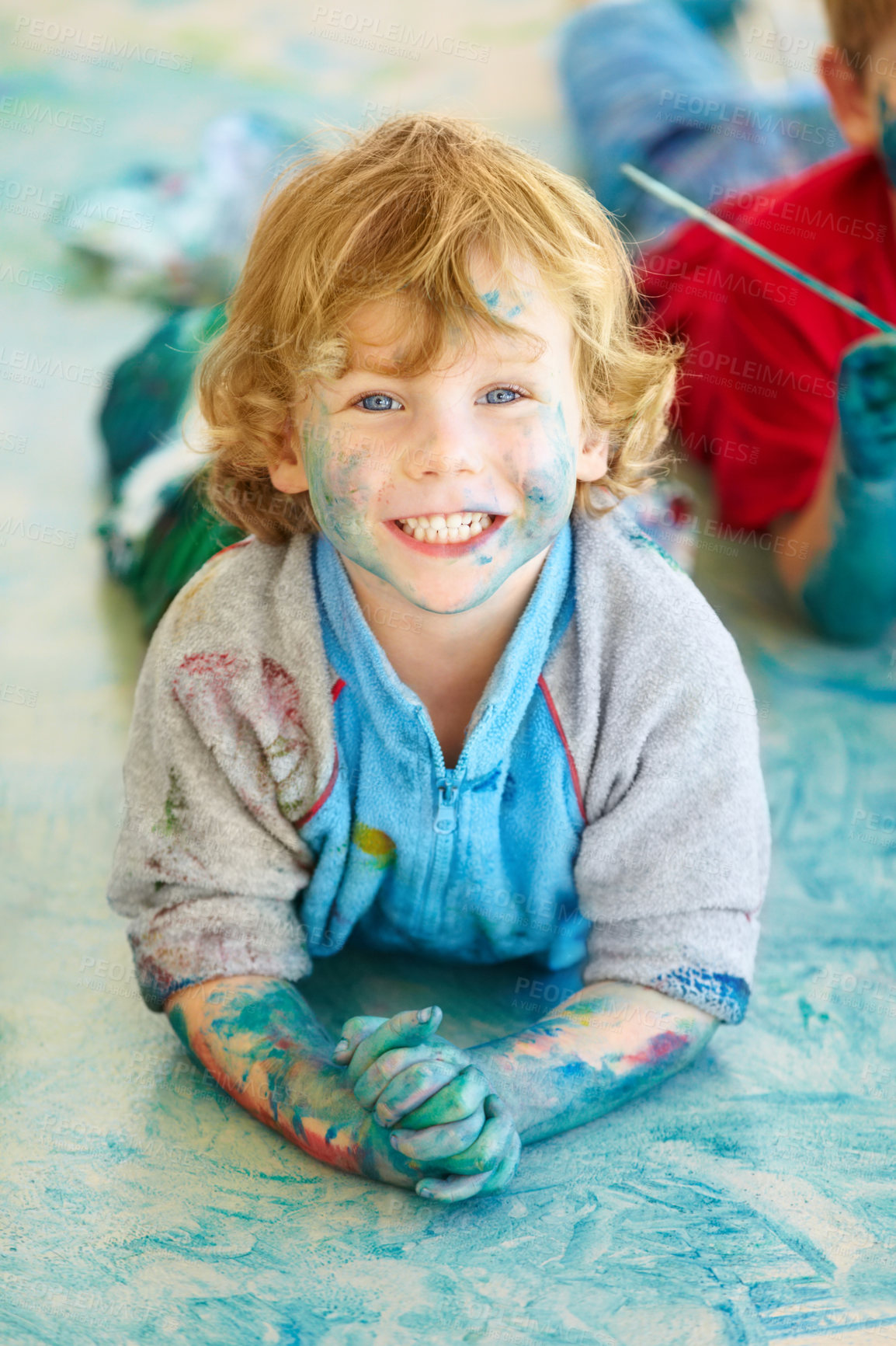 Buy stock photo Portrait, paint and a boy lying on the floor of a studio for creative expression or education at school. Art, painting and an excited young child looking happy with his messy artistic creativity