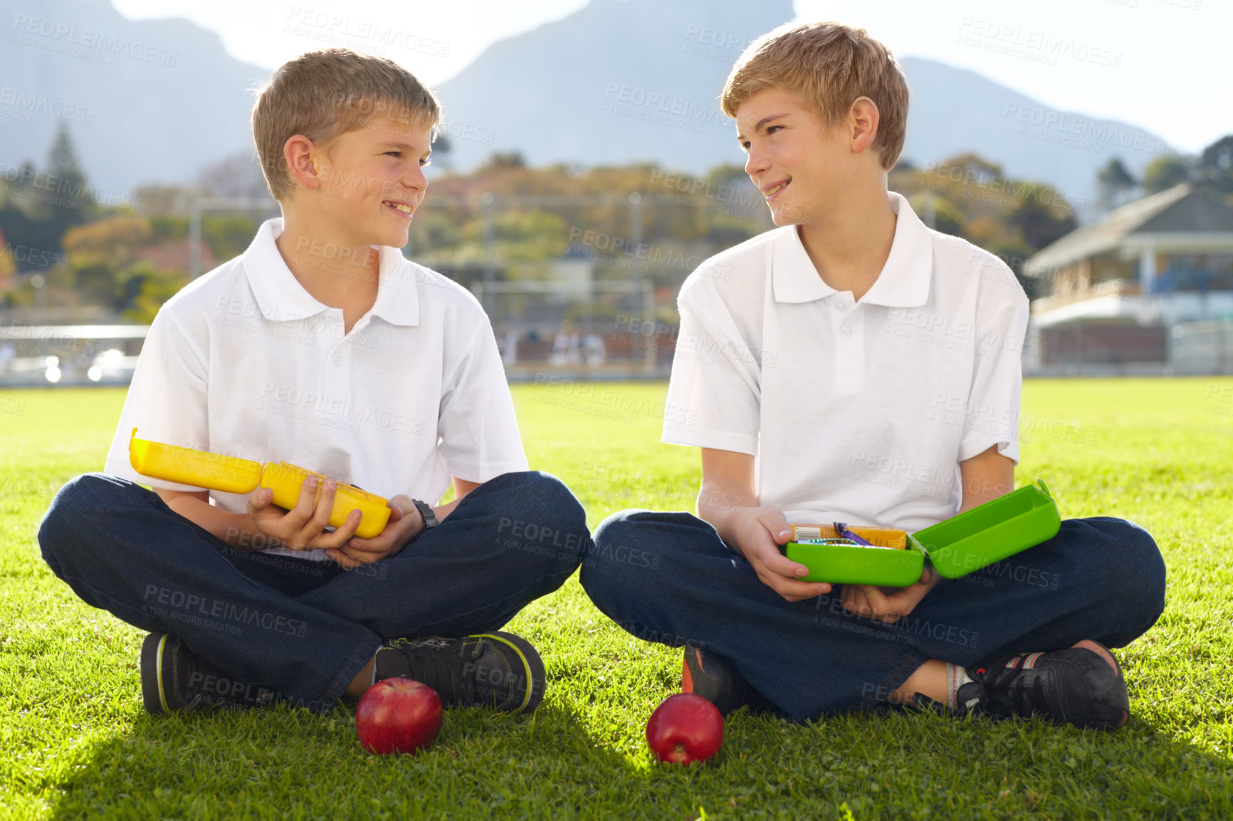Buy stock photo Two young schoolboys sitting on the grass about to eat their lunch