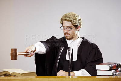 Buy stock photo Serious young judge sitting in the courtroom with a stern facial expression while holding out a gavel