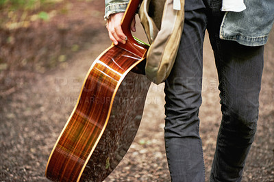 Buy stock photo A cropped closeup shot of a young man carrying a guitar while walking down a forest path