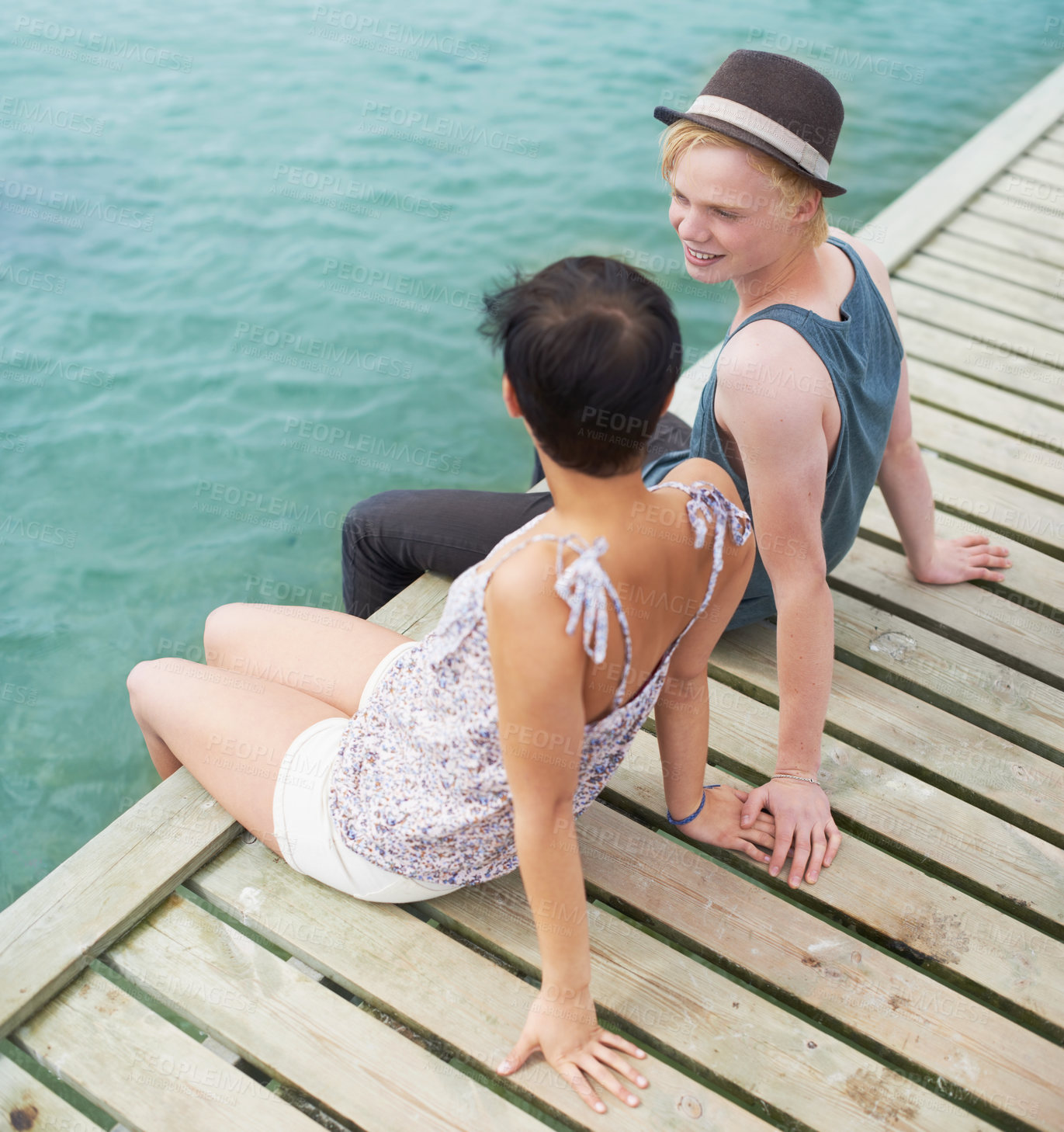 Buy stock photo A high angle shot of a young couple talking while sitting on a dock with their legs hanging over the edge