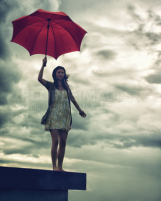 Buy stock photo Cute young woman holding an umbrella while standing on a rooftop