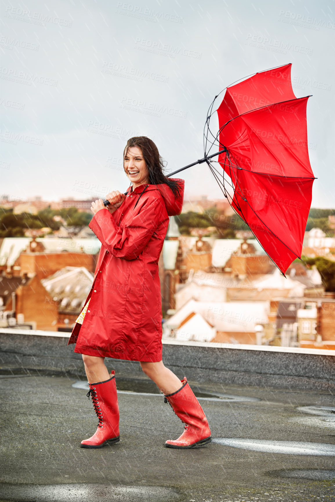 Buy stock photo Young woman laughing while being battered by rain and wind on a rooftop