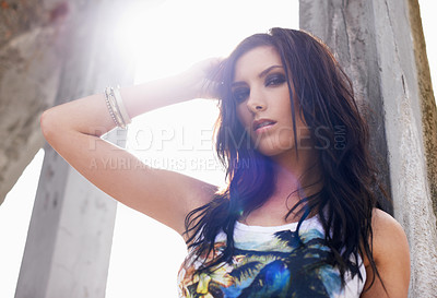 Buy stock photo Shot of a young woman standing with her hand in her hair in an urban setting