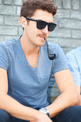 Buy stock photo Man in sunglasses, smoking pipe and thinking, relax outdoor and fashion in urban city by wall. Smoke, cool person in glasses or style, serious or hipster in casual clothes, tshirt and sitting in town