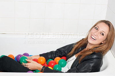 Buy stock photo Balls, funny and woman in bathtub for fashion, style and smile of trendy hipster at home. Laughing person in tub with color, sphere or plastic with body in bathroom, relax and cool clothes in Canada