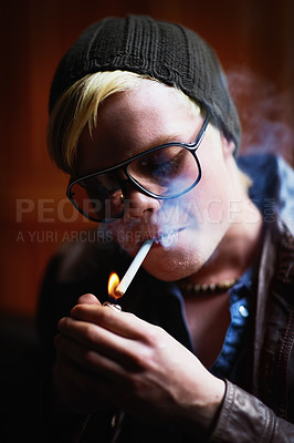 Buy stock photo Young guy in urban wear lighting up a cigarette