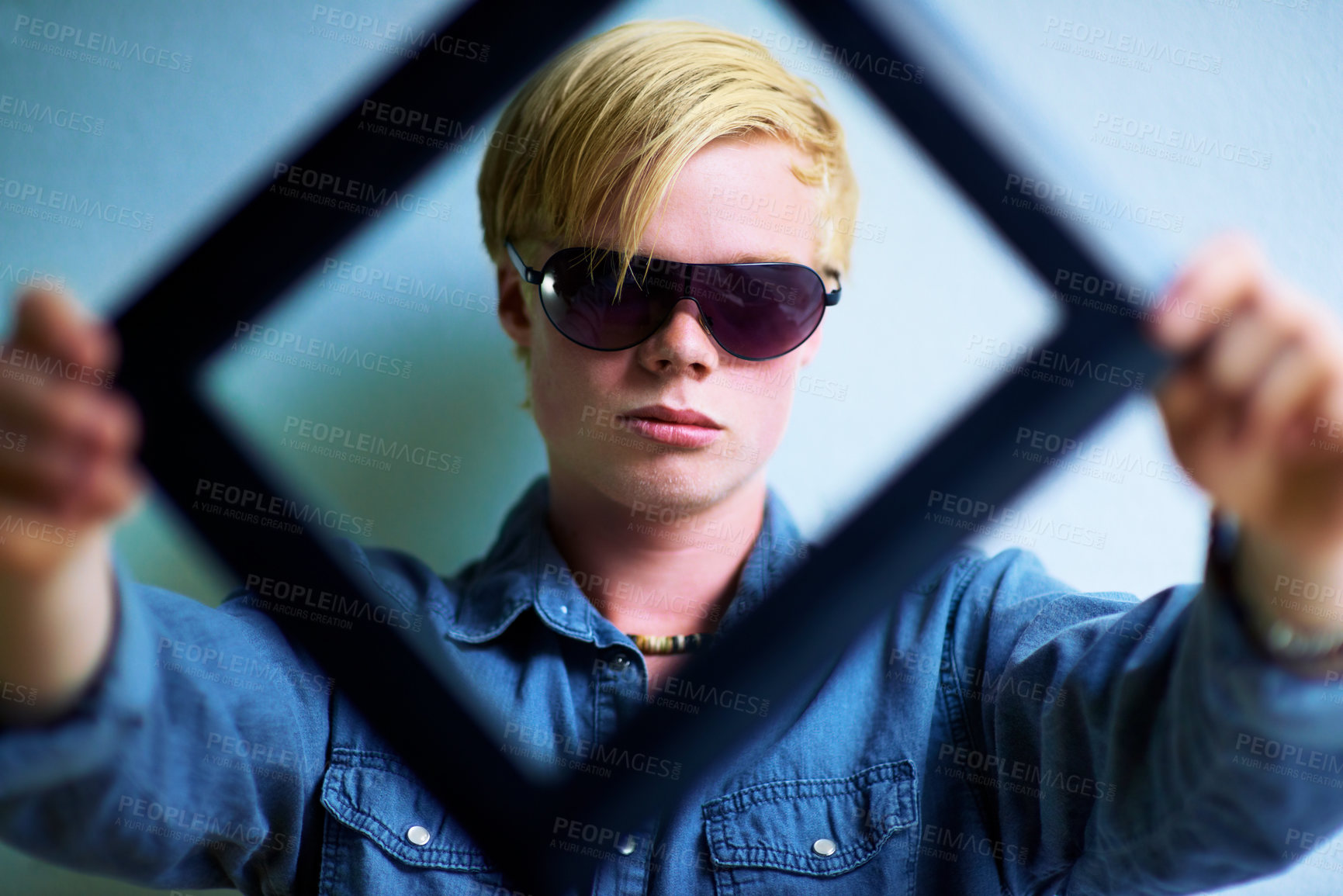 Buy stock photo Trendy young guy holding up a frame that frames his face