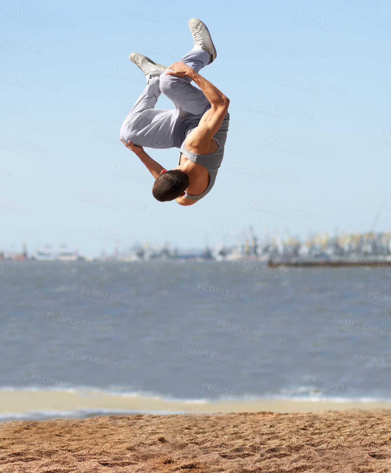 Buy stock photo An athletic young man doing a somersault at the beach