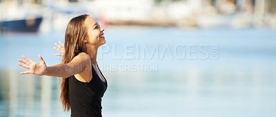 Buy stock photo A gorgeous young woman standing with arms outstretched at the harbour