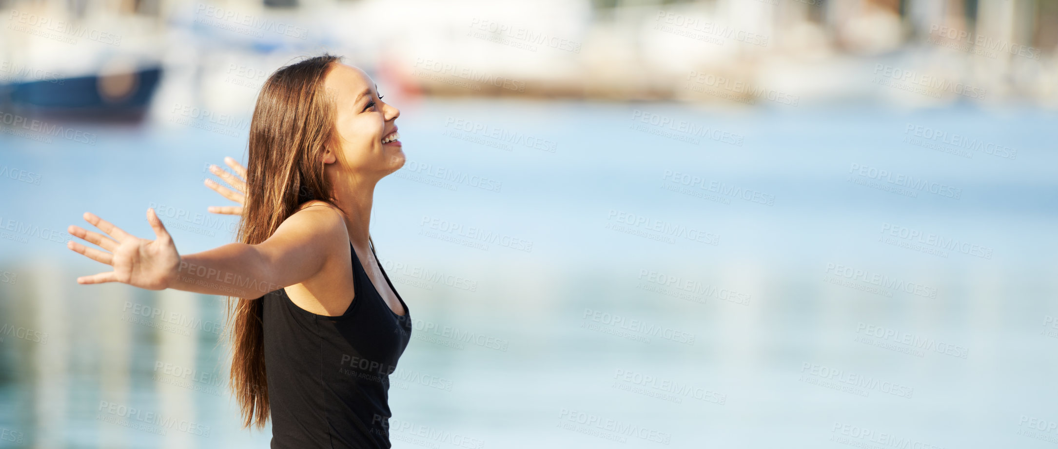 Buy stock photo A gorgeous young woman standing with arms outstretched at the harbour