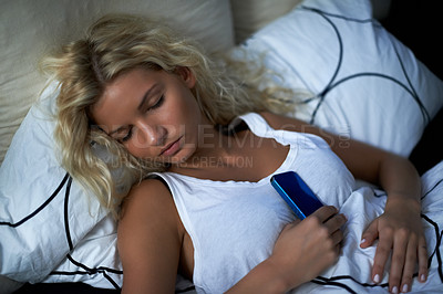 Buy stock photo Shot of a young woman sleeping while holding on to her cellphone
