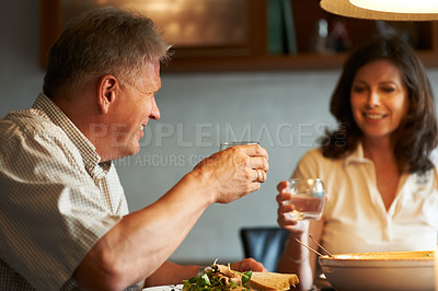 Buy stock photo Mature couple, cheers and eating together with wine, food and love in marriage with smile in home. Toast, old man and woman at dinner table with celebration, happiness and bonding date apartment.