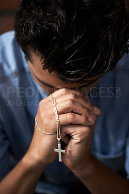Buy stock photo A young man bowing his head and holding a crucifix