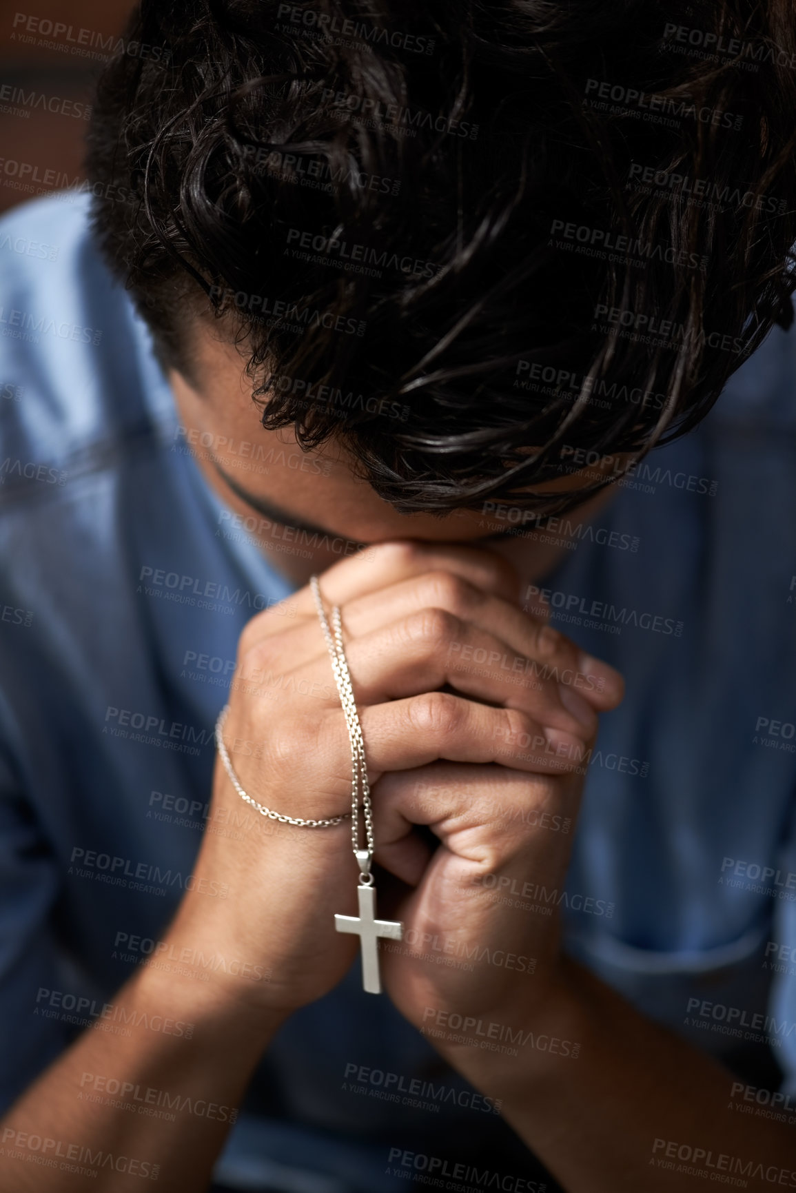 Buy stock photo A young man bowing his head and holding a crucifix