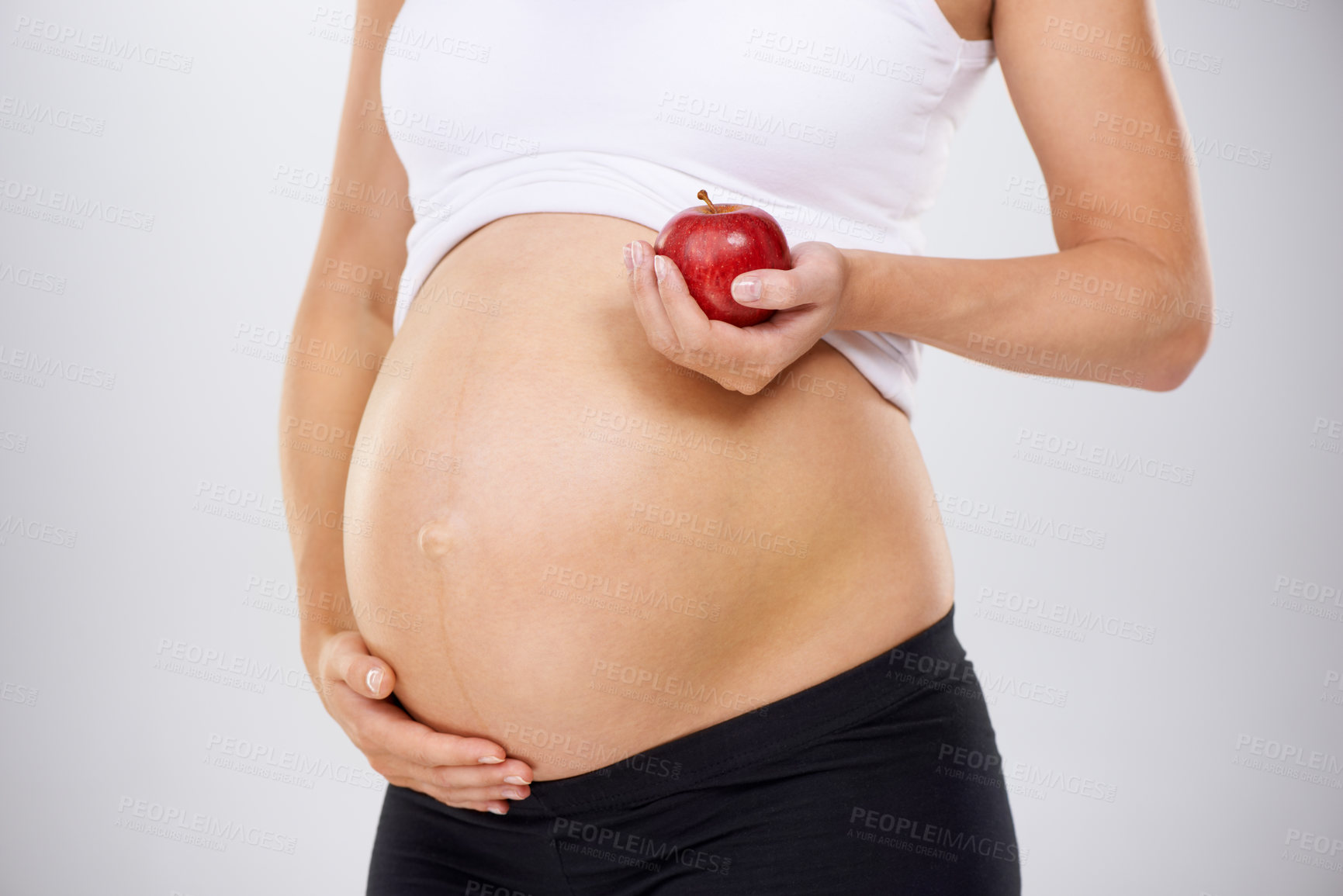 Buy stock photo Cropped image of a pregnant woman holding an apple and touching her stomach lovingly