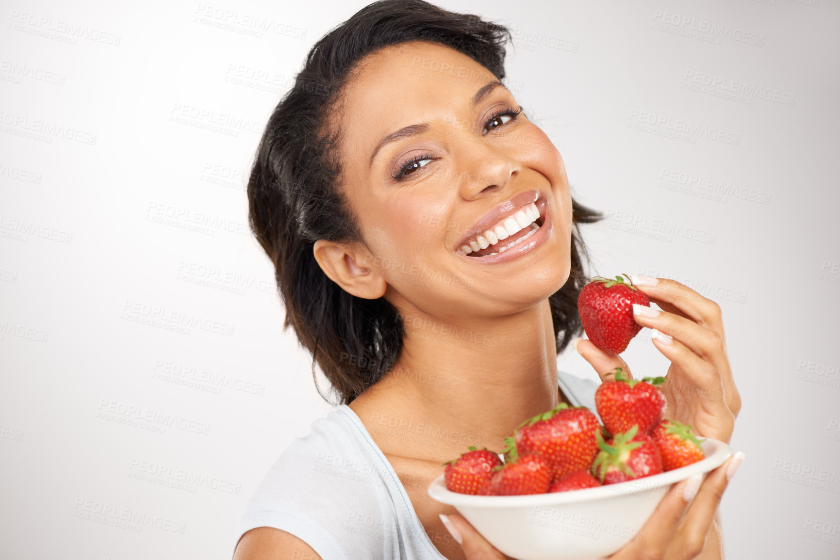 Buy stock photo Health, strawberries and young woman in a studio for wellness, nutrition and organic diet. Smile, vitamins and portrait of female person eating a fruit for healthy vegan snack by gray background.