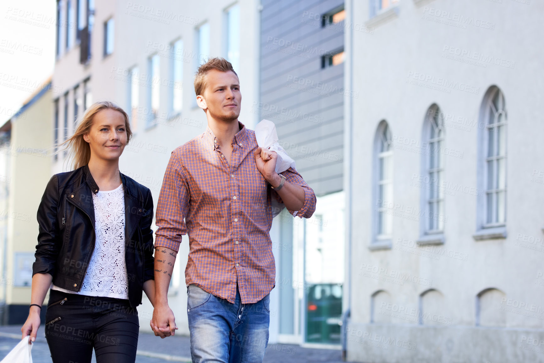 Buy stock photo A happy young couple walking hand in hand through the streets