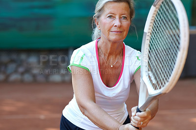 Buy stock photo Senior woman preparing to return a serve during a game of tennis