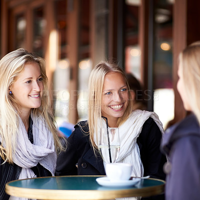 Buy stock photo Three friends seated at a coffee shop talking to each other and smiling