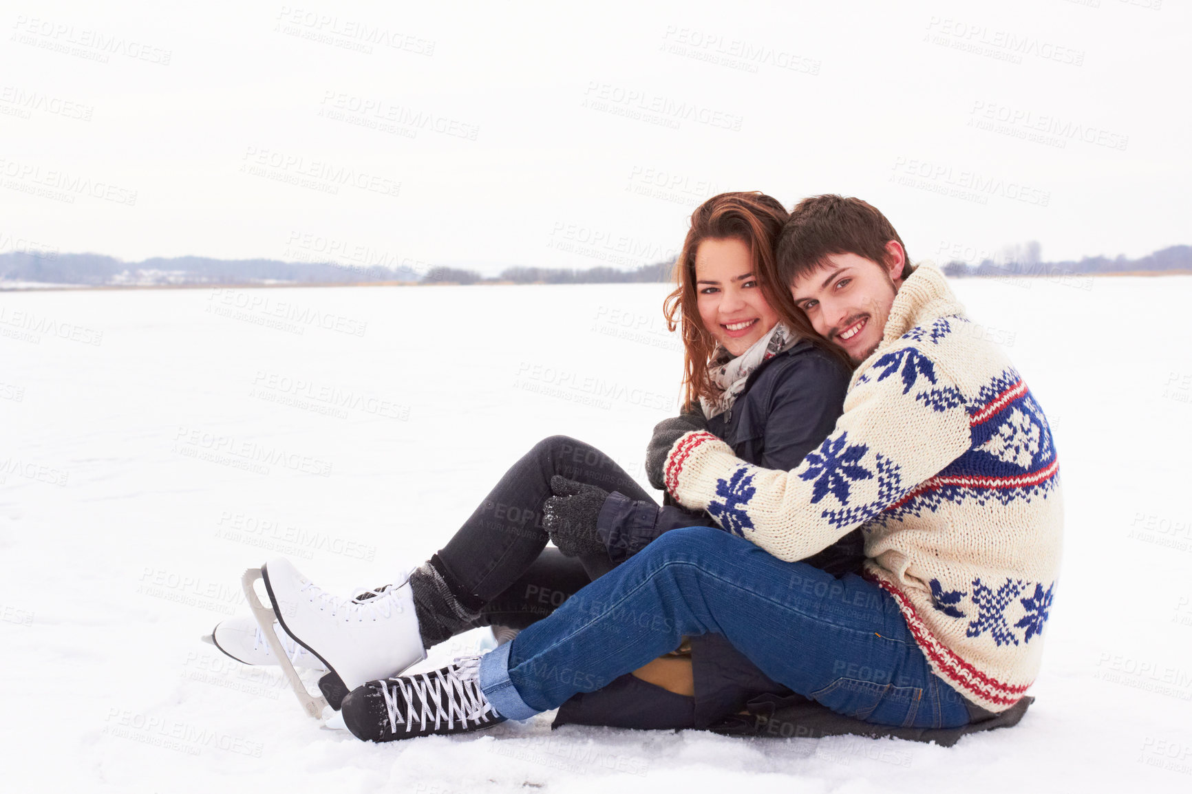 Buy stock photo Sweet young couple in ice skates cuddling on the ice of a frozen natural lake outdoors