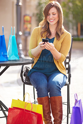 Buy stock photo Shot of an attractive young woman texting a friend about all the bargains she found