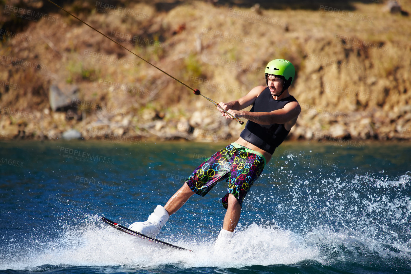 Buy stock photo A young man wearing a helmet and lifejacket wakeboarding on a lake