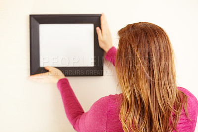 Buy stock photo Rearview shot of a woman placing an empty frame on a wall