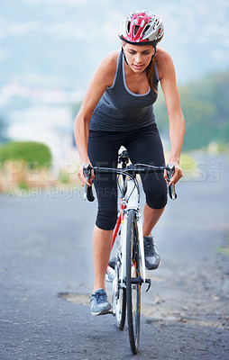 Buy stock photo Cropped shot of a lone female cyclist riding uphill on a rural road