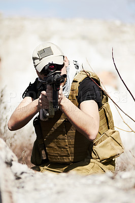 Buy stock photo A soldier crouched down and pointing his gun at the camera during a training in a desert environment