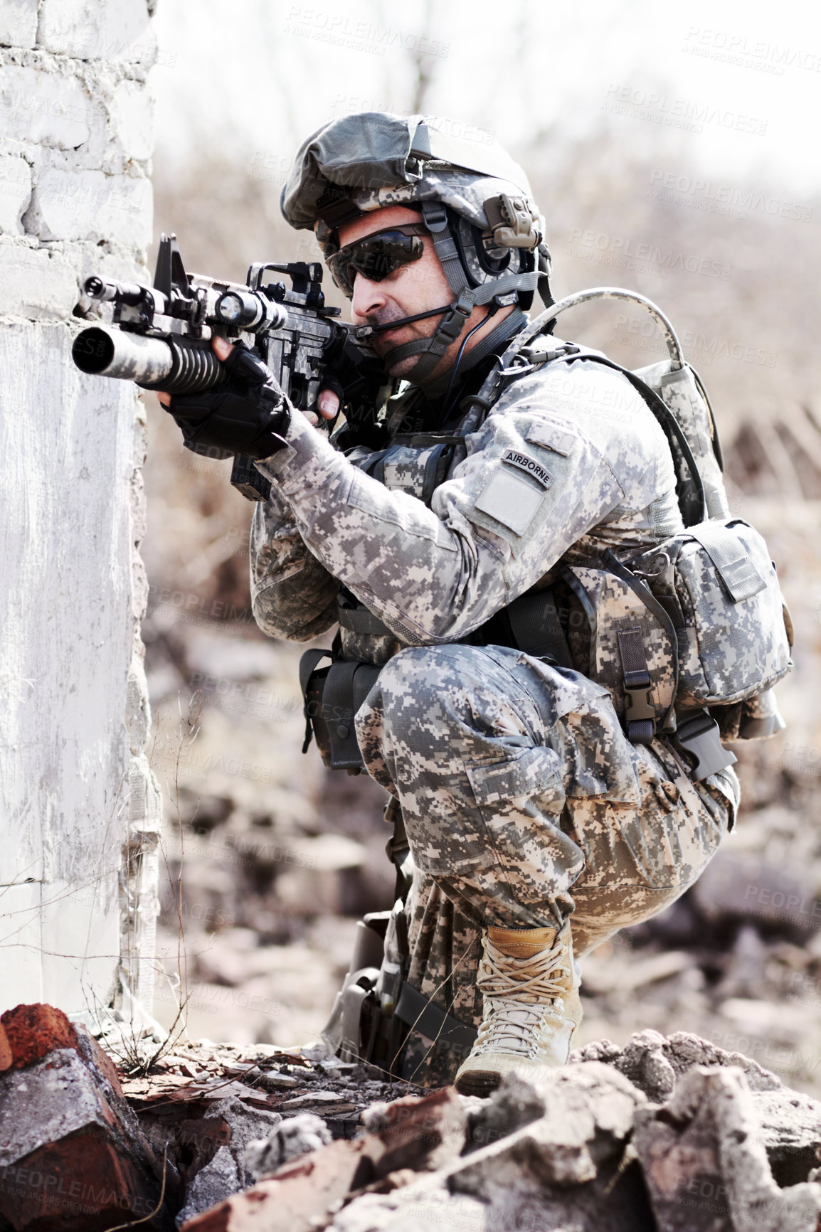 Buy stock photo A soldier crouched down next to a broken down wall and pointing his gun into the distance