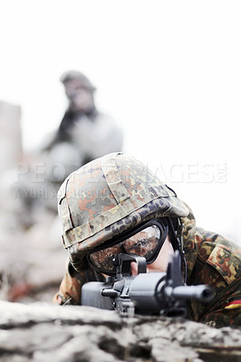Buy stock photo Closeup of a soldier peering over a mound of stones and pointing his gun at the camera with copyspace