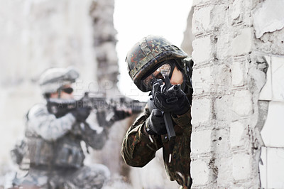 Buy stock photo A soldier peering around a wall while pointing a gun at the camera during a rade on a damaged building