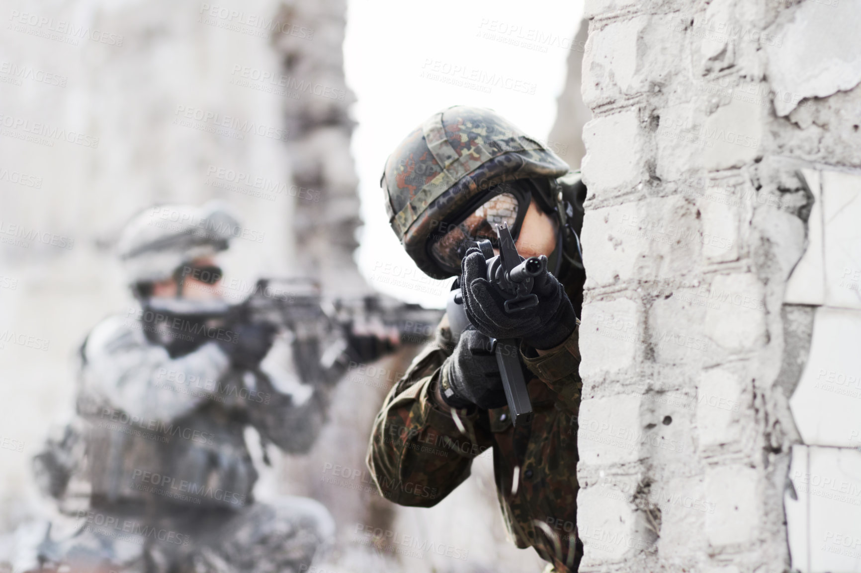 Buy stock photo A soldier peering around a wall while pointing a gun at the camera during a rade on a damaged building