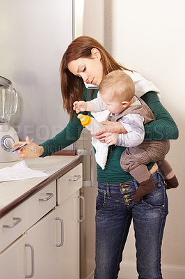 Buy stock photo Young mom trying to multi-task while holding her baby son and his bottle