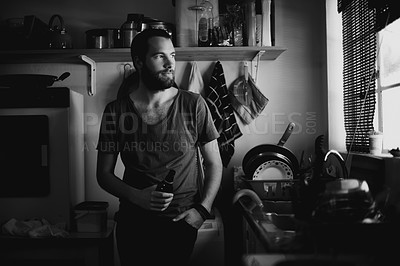Buy stock photo A young man looking out of his kitchen window thoughtfully while enjoying a beer