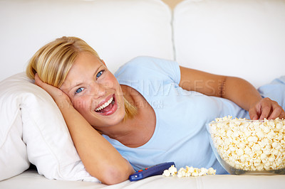 Buy stock photo Young woman lying on the couch and watching TV while eating popcorn