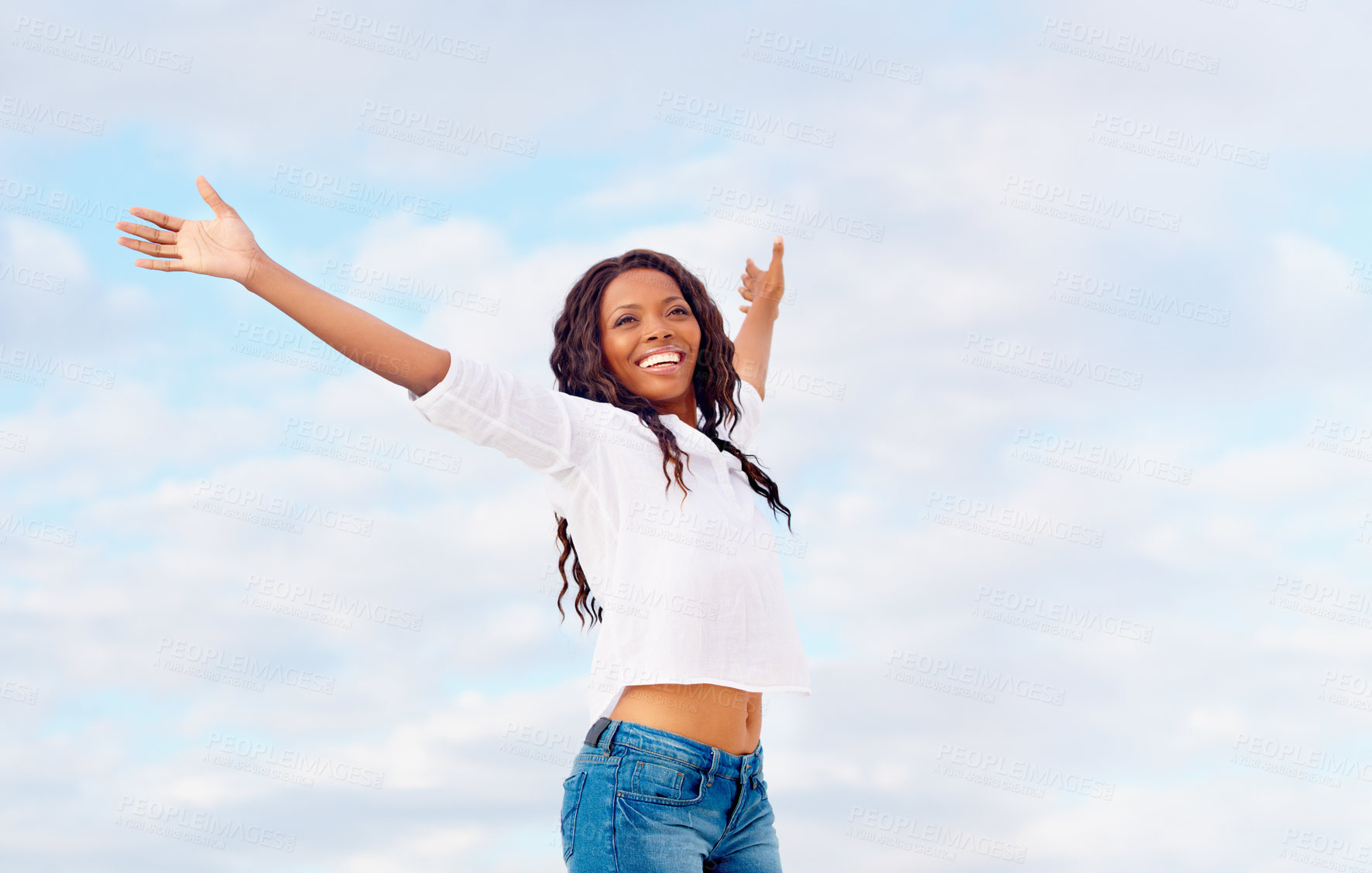 Buy stock photo Happy young woman standing against a blue sky with her arms outstretched