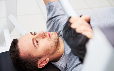 Buy stock photo A young man bench-pressing at the gym