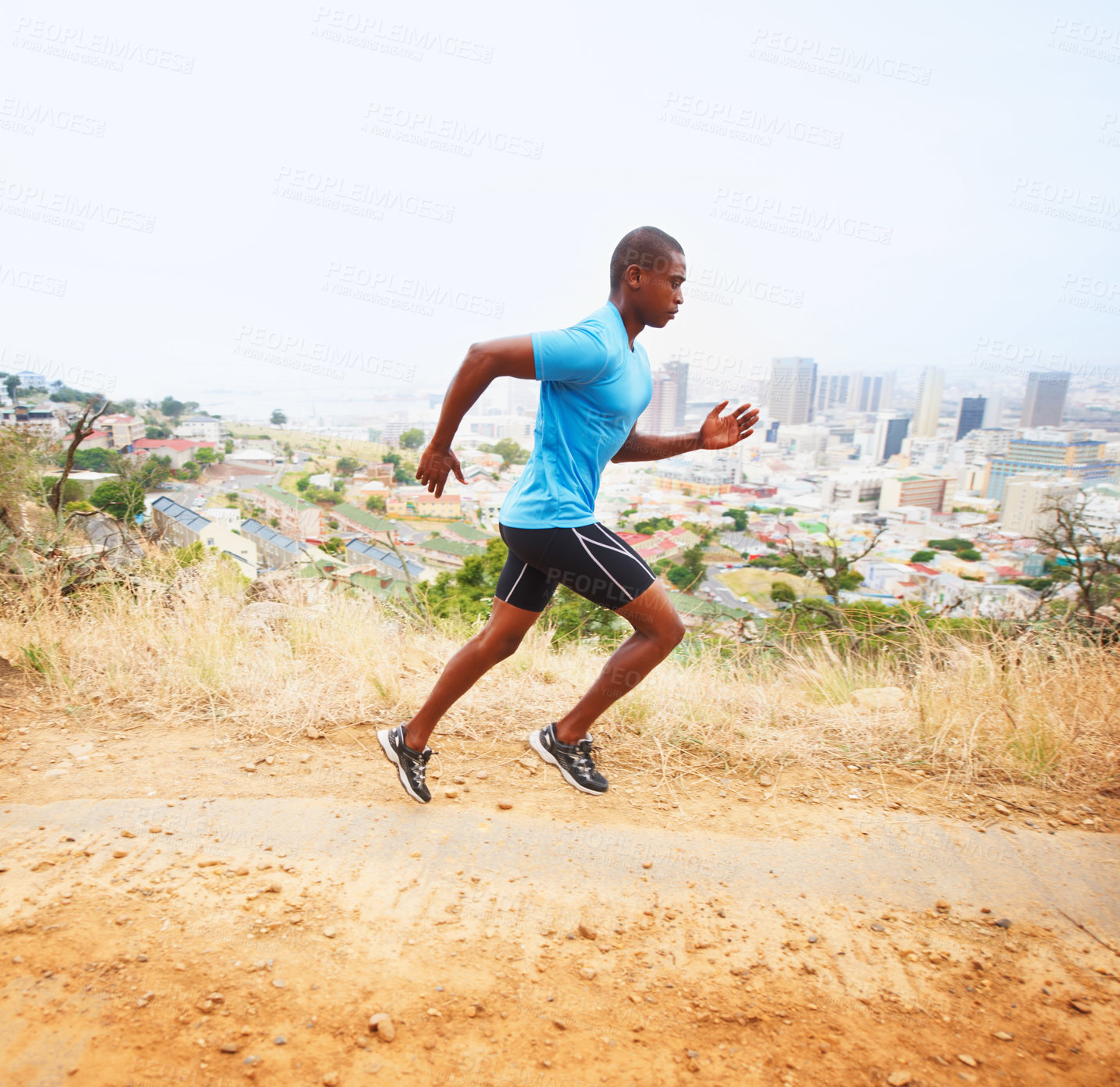 Buy stock photo A young man running along a nature trail with the city in the background