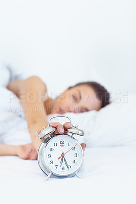 Buy stock photo Shot of a sleepy young woman reaching out to turn off her alarm clock