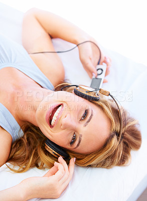 Buy stock photo Young woman listening to music while wearing a pair of headphones and smiling