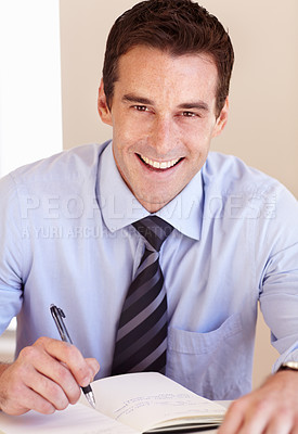 Buy stock photo Smiling young businessman filling in his dayplanner