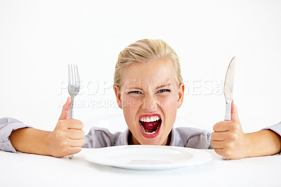 Buy stock photo Furious young woman sitting in front of an empty plate while holding her knife and fork