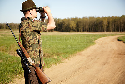 Buy stock photo A game ranger with his rifle looking through his binoculars in the outdoors with copyspace