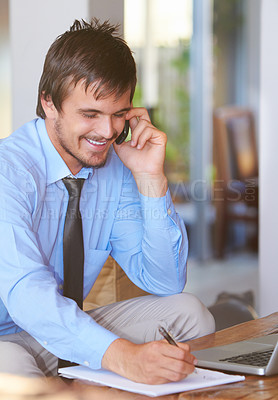 Buy stock photo Shot of a young businessman talking on the phone while sitting in front of his laptop