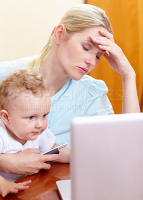 Buy stock photo A mother looking overwhelmed sitting in front of the computer with her baby