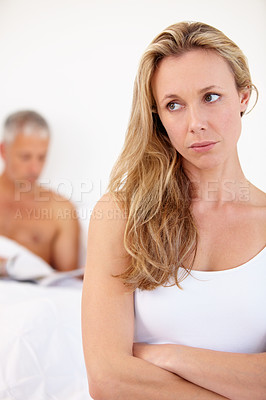 Buy stock photo An unhappy wife sitting at the edge of her bed with her husband sitting in the background