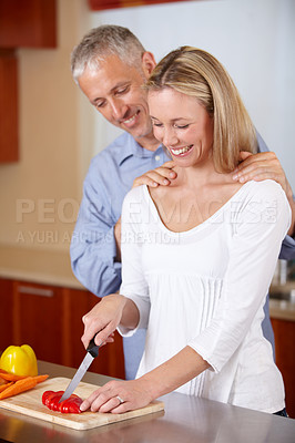 Buy stock photo A husband looking over his wife&#039;s shoulder as she&#039;s chopping up peppers for a meal